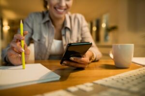 a smiling woman using a smartphone while learning in the evening at home