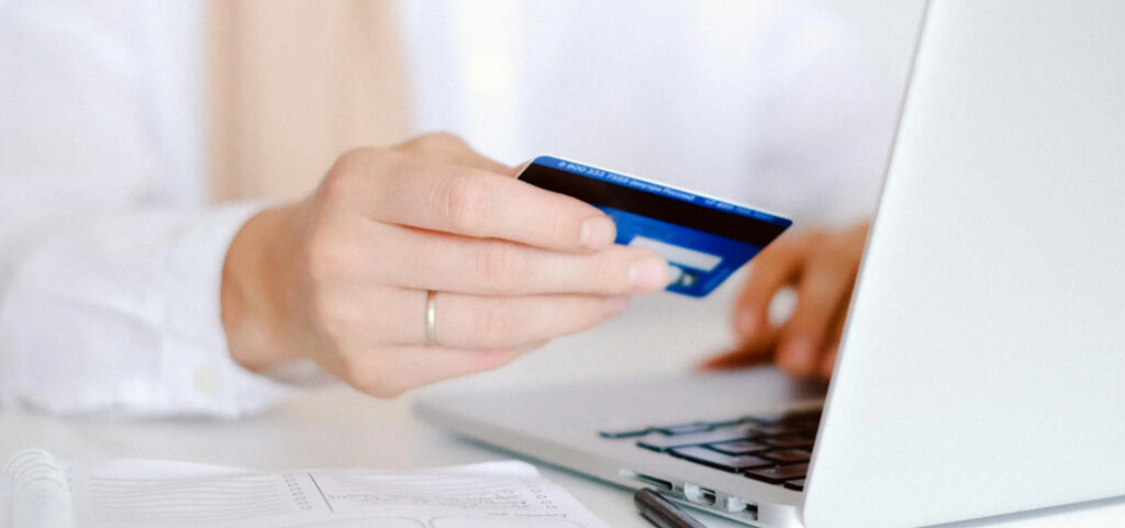 A person's hands holding a blue credit card over a laptop keyboard