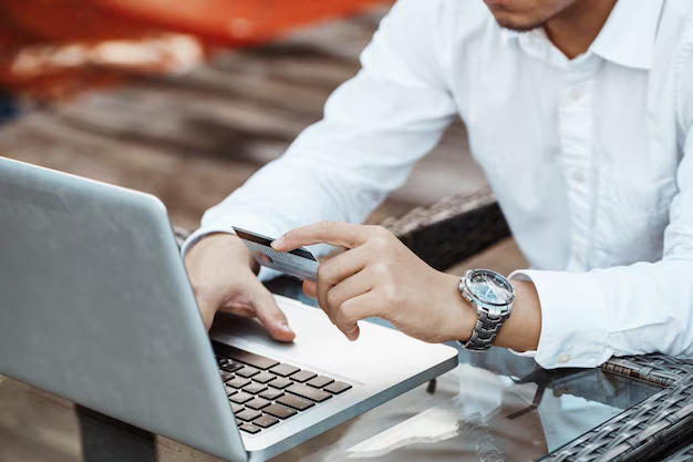 A man sitting at a laptop holds a bank card in his hands