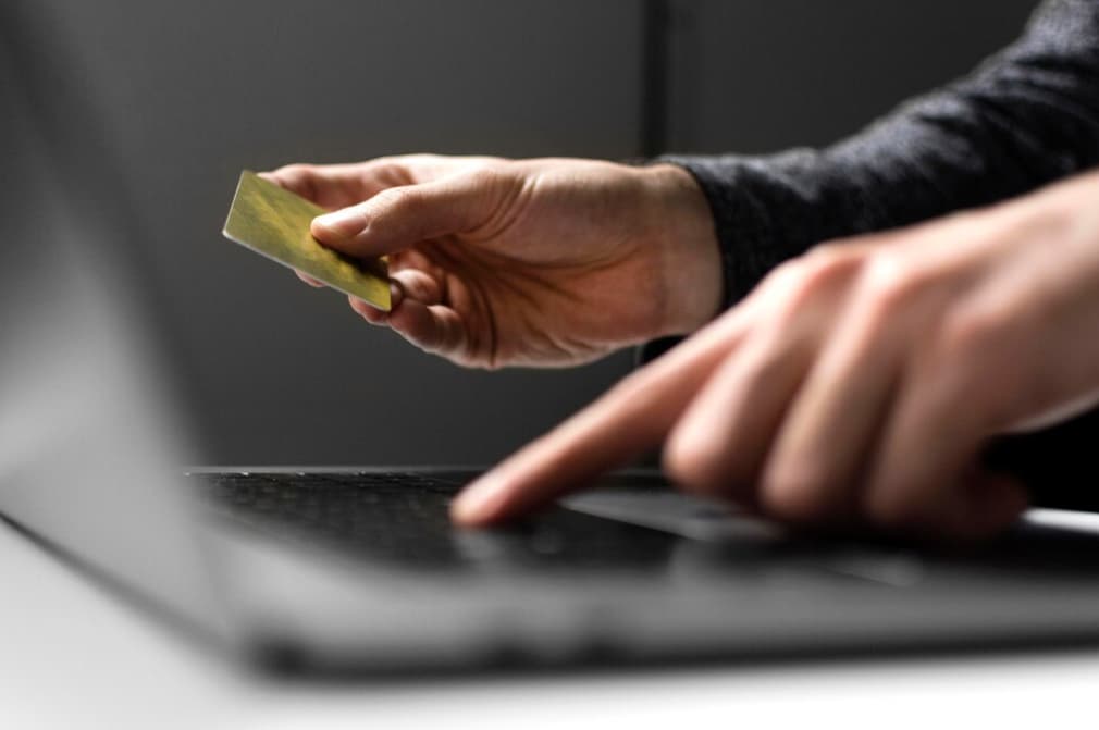 a hand holding a credit card near a laptop