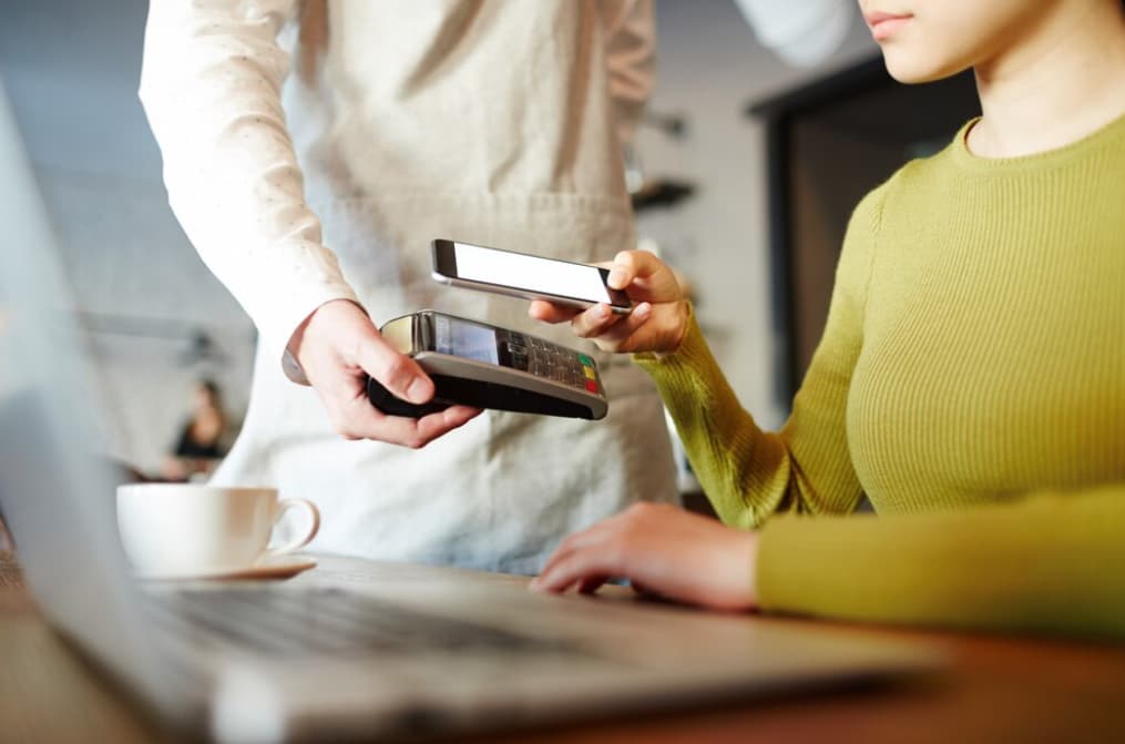 Customer tapping a phone to a payment device at a cafe counter